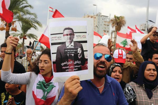 لبنانيون يرفعون الأعلام ولافتة محافظ «المركزي» في مظاهرة مناهضة للحكومة (رويترز)