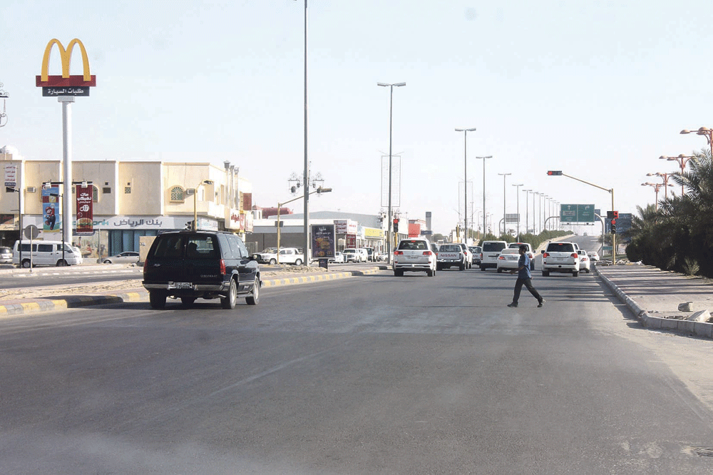 عامل ينتهز توقف الإشارة لعبور الشارع بسلام (تصوير: بدر الدوسري)