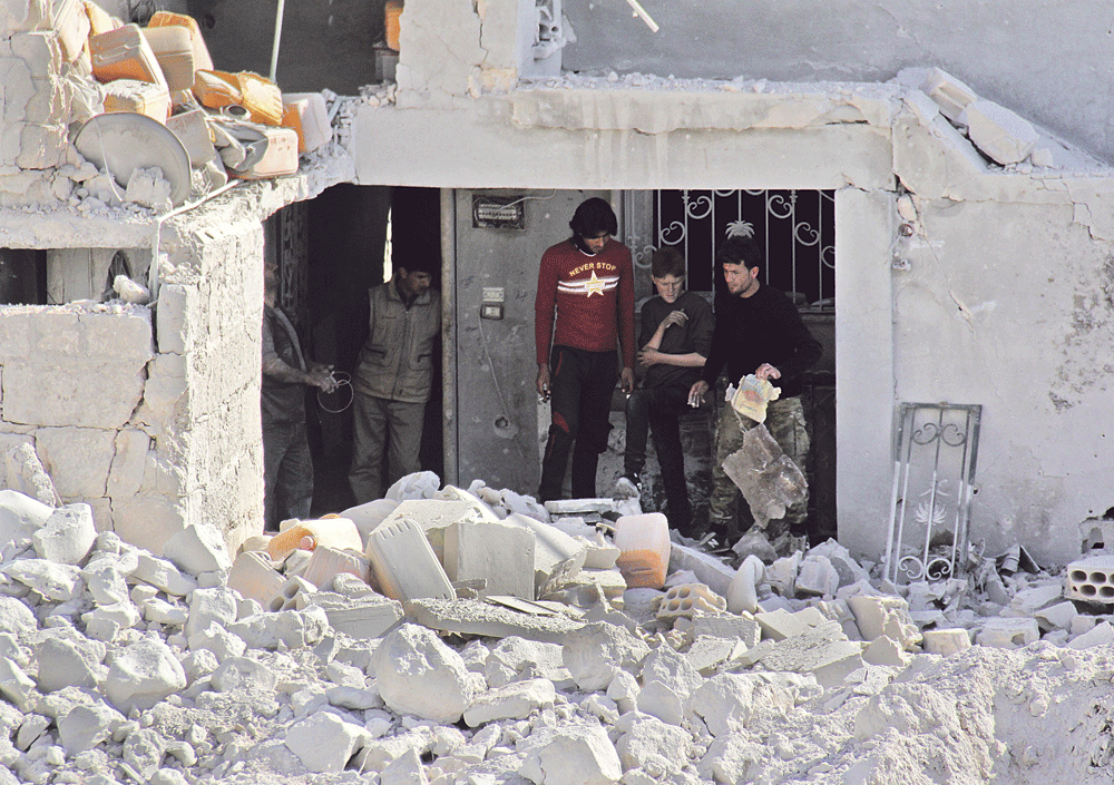 سوريون يبحثون عن أشيائهم وسط انقاض مبنى دمرته غارات الأسد في إدلب (أ.ف.ب)